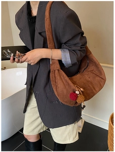 Brown suede crescent hobo bag with colorful pompom charm shown on a female model