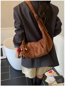 Detail of a brown suede hobo bag featuring colorful pom-pom charms and a wide shoulder strap