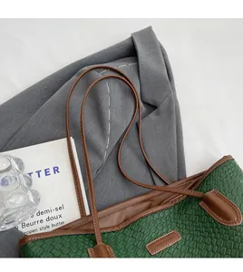 Detail of dark green woven tote bag with brown leather handles on a grey suit jacket