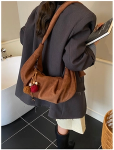 Close-up of brown suede crescent shoulder bag featuring stylish pleats and tassels