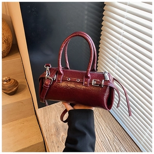 Detail of dark red patent leather cylindrical bag with silver eyelets and adjustable strap