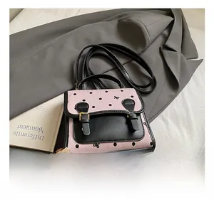 Detail view of a retro pink and black polka dot crossbody bag with gold buckles