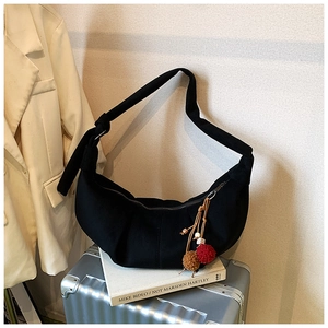 Detail of black canvas crescent shoulder bag with dark red and brown plush ball pendants