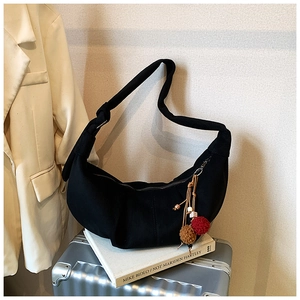 Detail of a black pleated crescent shoulder bag with a colorful plush ball charm