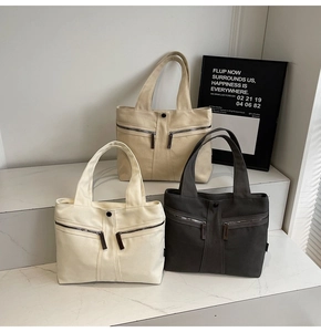 Three minimalist canvas tote bags in beige, khaki, and dark grey with front zipper pockets