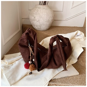 Detail of dark brown suede crescent bag with knotted strap and fuzzy pompom charm