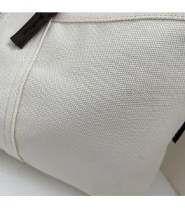 Close-up of off-white canvas fabric texture with dark brown leather zipper puller detail