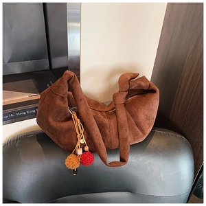 Detail of dark brown suede shoulder bag with knot strap and colorful pompom pendant