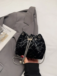 Detail of black quilted bucket bag featuring silver chain strap and pearl charm pendant