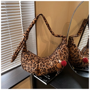 Detail of leopard print crescent bag featuring a knotted shoulder strap and plush pompom charms