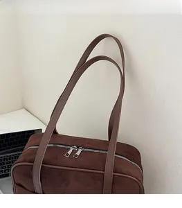 Detail of a brown suede tote bag featuring a durable zipper and smooth shoulder strap