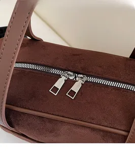 Close-up of dual silver metal zippers on dark brown suede cylindrical shoulder bag