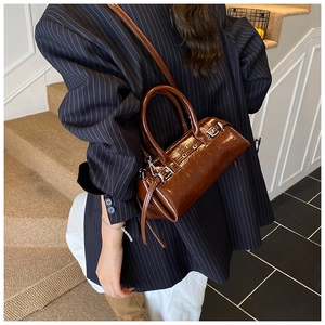Close-up of caramel brown glossy shoulder bag with silver buckle and eyelet details
