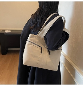 Side view of beige canvas tote bag with front zipper pocket shown on a model