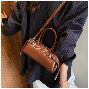 Detail of dark brown polished leather cylinder bag with silver buckles worn by a model