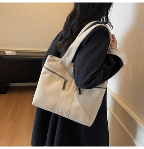 Side view of a spacious off-white canvas tote bag with front zipper detail and wide shoulder strap