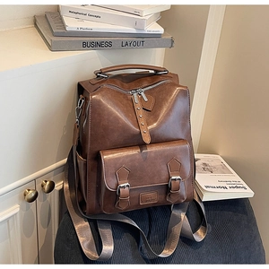 Detail of vintage brown leather backpack showing zippers and buckle pockets on wood cabinet
