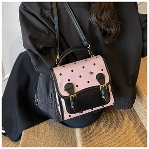 Detail of pink polka dot handbag with black leather straps and gold buckle on model