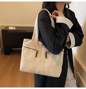 Detail of off-white canvas tote bag featuring dual front metal zipper pockets for storage
