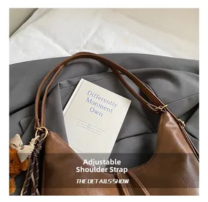 Detail of brown leather dumpling bag with adjustable strap and cute bear charm pendant