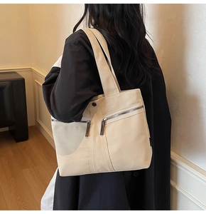 Detail view of beige canvas tote bag with dual zipper pockets and leather pulls