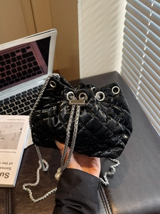 Detail of black quilted patent leather bucket bag with silver chain and pearl charm