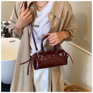 Deep red patent leather baguette bag with silver buckles shown in a lifestyle model shot