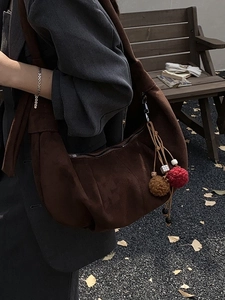 Brown faux suede hobo bag with colorful pompom charm shown in a fall setting