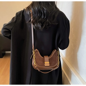 Détail d'un sac demi-lune marron foncé avec boucle dorée sur un blazer noir chic