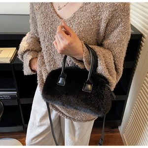 Detailed view of a black faux fur handbag with dual leather handles and a slim shoulder strap