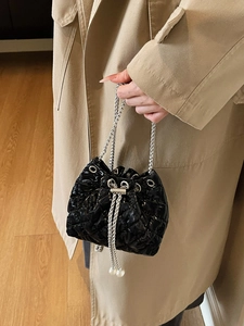 Detail of black quilted bucket bag with chain strap and pearl drawstring accents