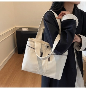 Detailed shot of cream canvas tote bag with dual zipper pockets on shoulder strap