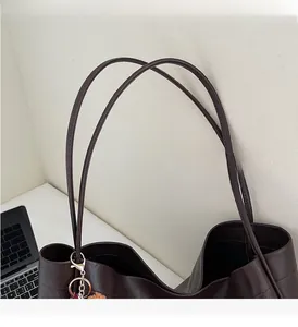 Detail of dark brown tote bag handle with sturdy metal hooks and plush ball pendant