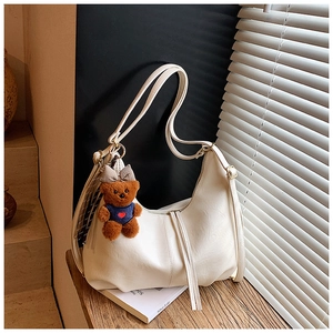 Close-up of beige hobo bag with teddy bear charm and plaid scarf on a windowsill