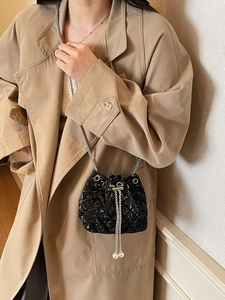 Close-up of black quilted bucket bag featuring a silver chain and elegant pearl pendant