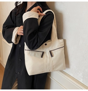 Detail view of large beige canvas tote bag with front zippers and metal snap button