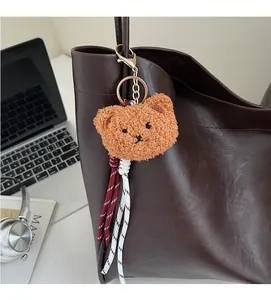 Close-up of a brown plush bear charm with woven tassels on a leather tote bag