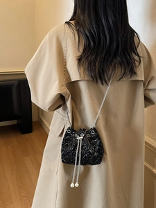Detail of a quilted black bucket bag with silver chain and elegant pearl tassels