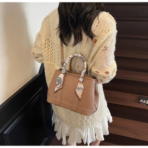 Close-up of brown lychee leather bucket bag with silk scarf handle on model