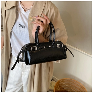 Detail of a vintage black patent leather baguette bag with silver buckle and belt straps