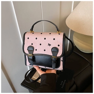Detailed view of pink polka dot handbag with black leather flap and metallic buckles
