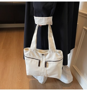 Detail of off-white canvas tote bag featuring dual front zipper pockets and minimalist design