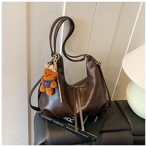 Detail of dark brown pleated dumpling bag with a cute bear charm on a coffee table