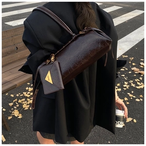 Detail of dark brown wax leather cylindrical bag with matching mini pouch and metal accents
