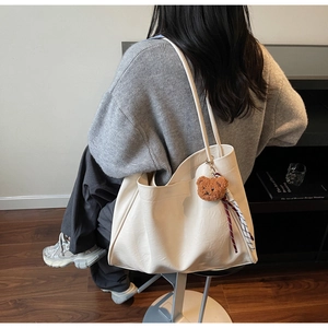 Detail of white leather tote bag with plush bear charm on model for commuting style