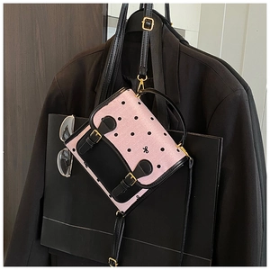 Detail view of pink polka dot bag with black leather straps and metal buckle decoration