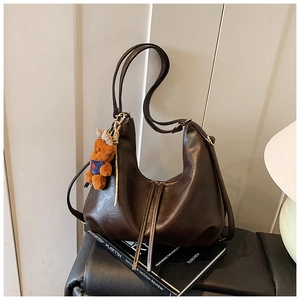 Detail of dark brown hobo bag with plush bear charm on a book against a striped wall