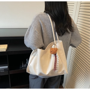 Detail of a creamy white textured tote bag featuring a cute brown plush bear charm