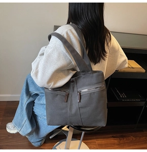 Detail of a large dark grey canvas tote bag with dual front zipper pockets and leather pulls