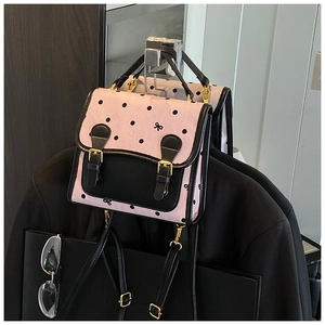 Detailed view of pink polka dot backpack with black leather trim and golden metal buckles